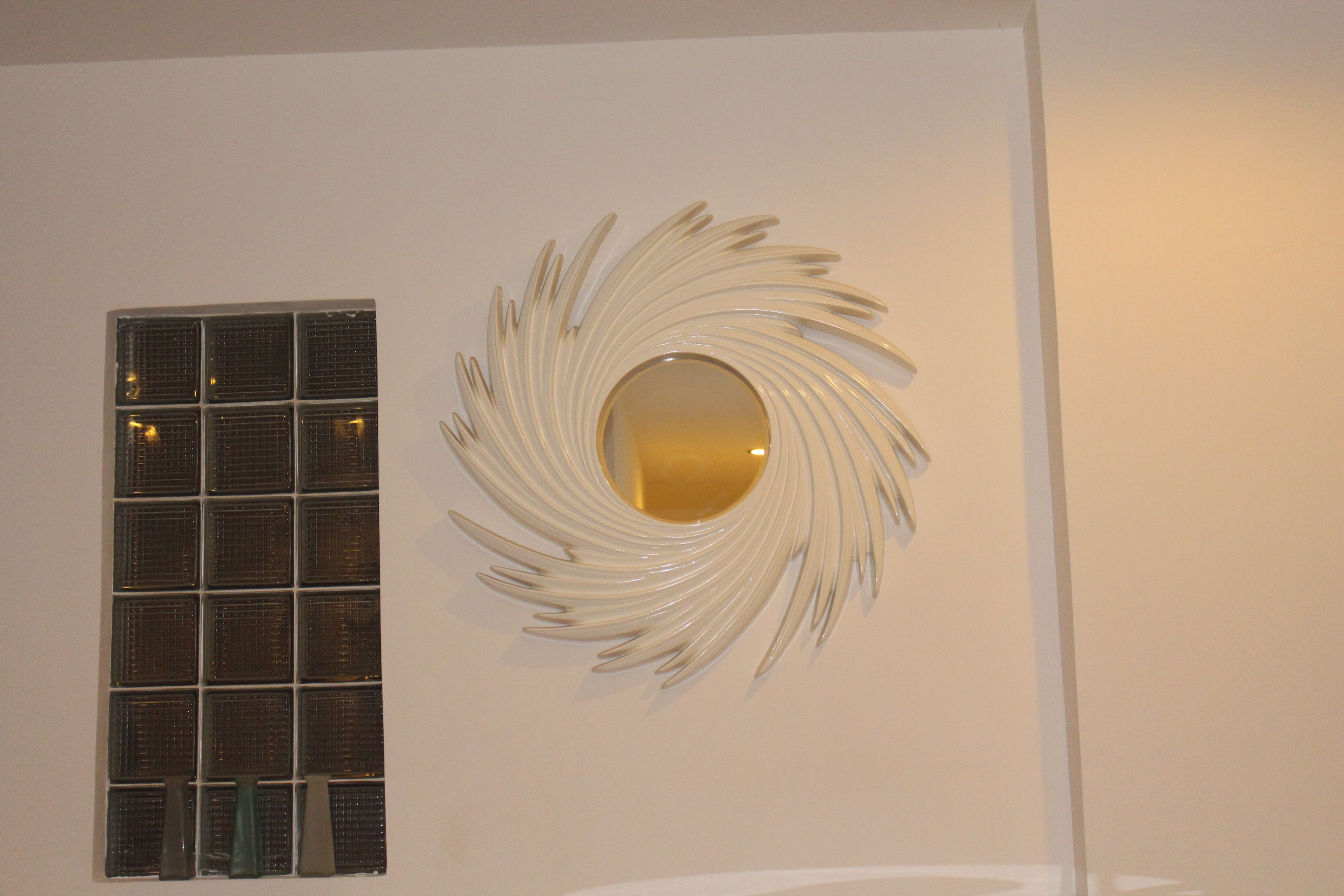 A wall with a circular mirror and a window with blinds.