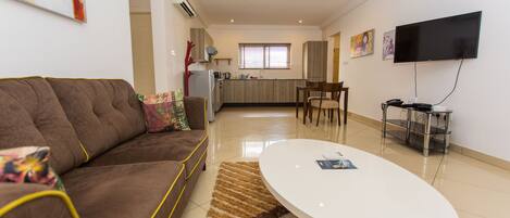 A modern living room with a brown sofa, a white coffee table, and a kitchen in the background.