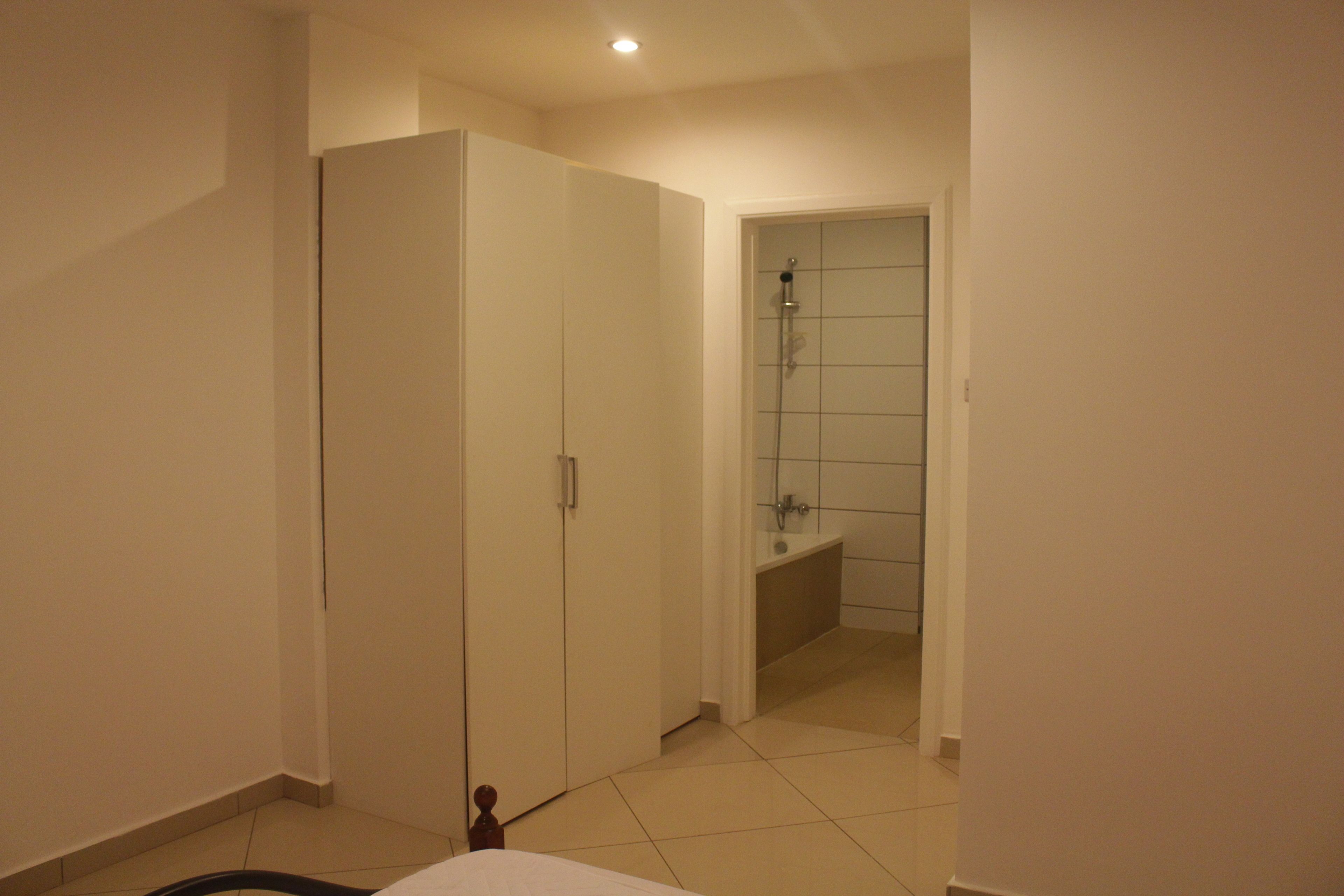 A bedroom with a bed, a wardrobe, and a bathroom with a shower.