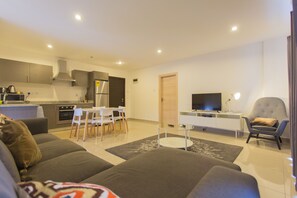 A modern living room with a sofa, a TV, and a dining area with chairs and a table. - Accra Luxury Apartments at The Gallery (Accra)