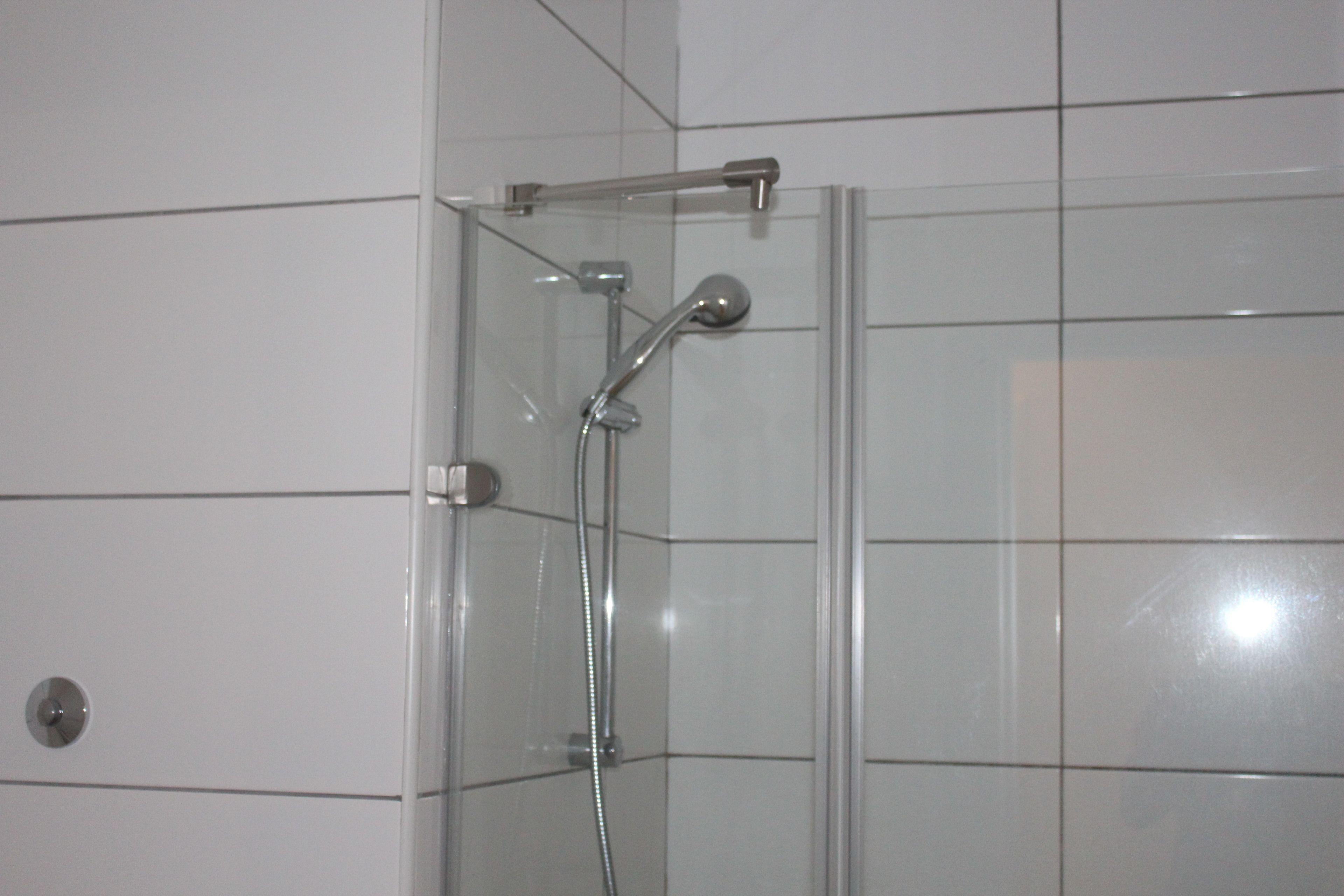 A glass-enclosed shower with a handheld showerhead and a wall-mounted faucet.