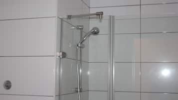 A glass-enclosed shower with a handheld showerhead and a wall-mounted faucet.