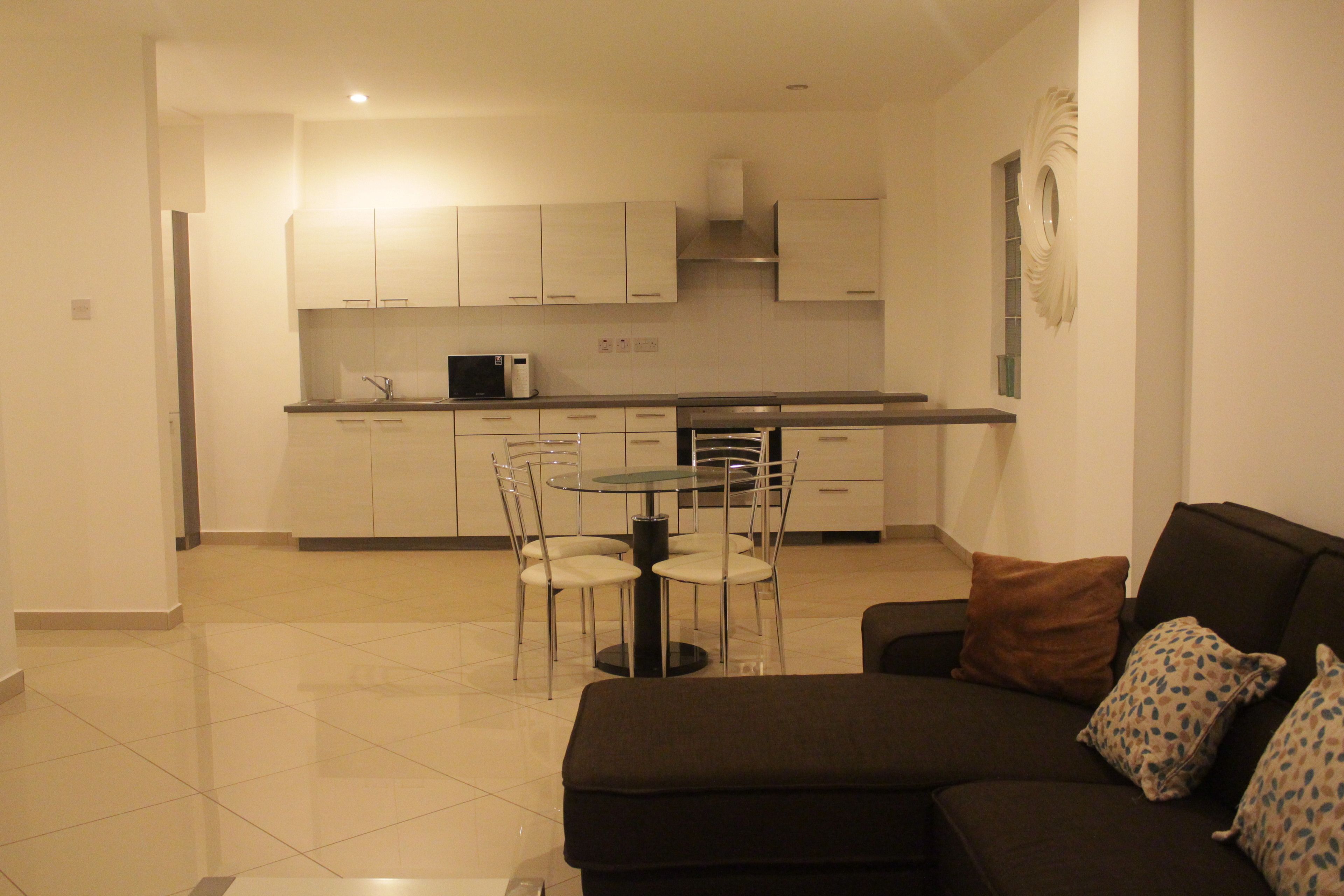 A modern kitchen with white cabinets, a dining table with chairs, and a black sofa with patterned cushions.