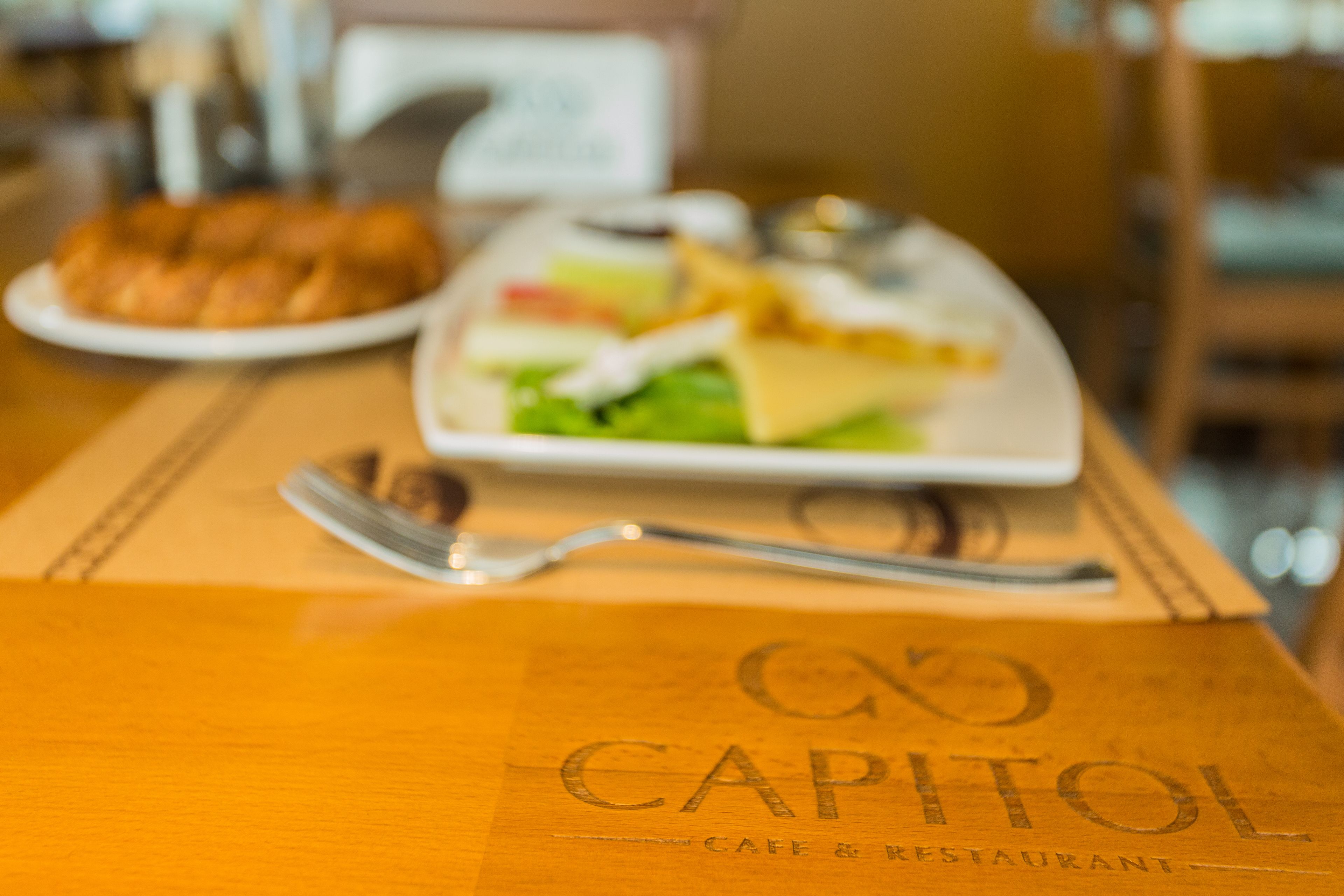 A wooden table with a plate of food and a fork. The table has a logo that reads "CAPITOL CAFE & RESTAURANT".