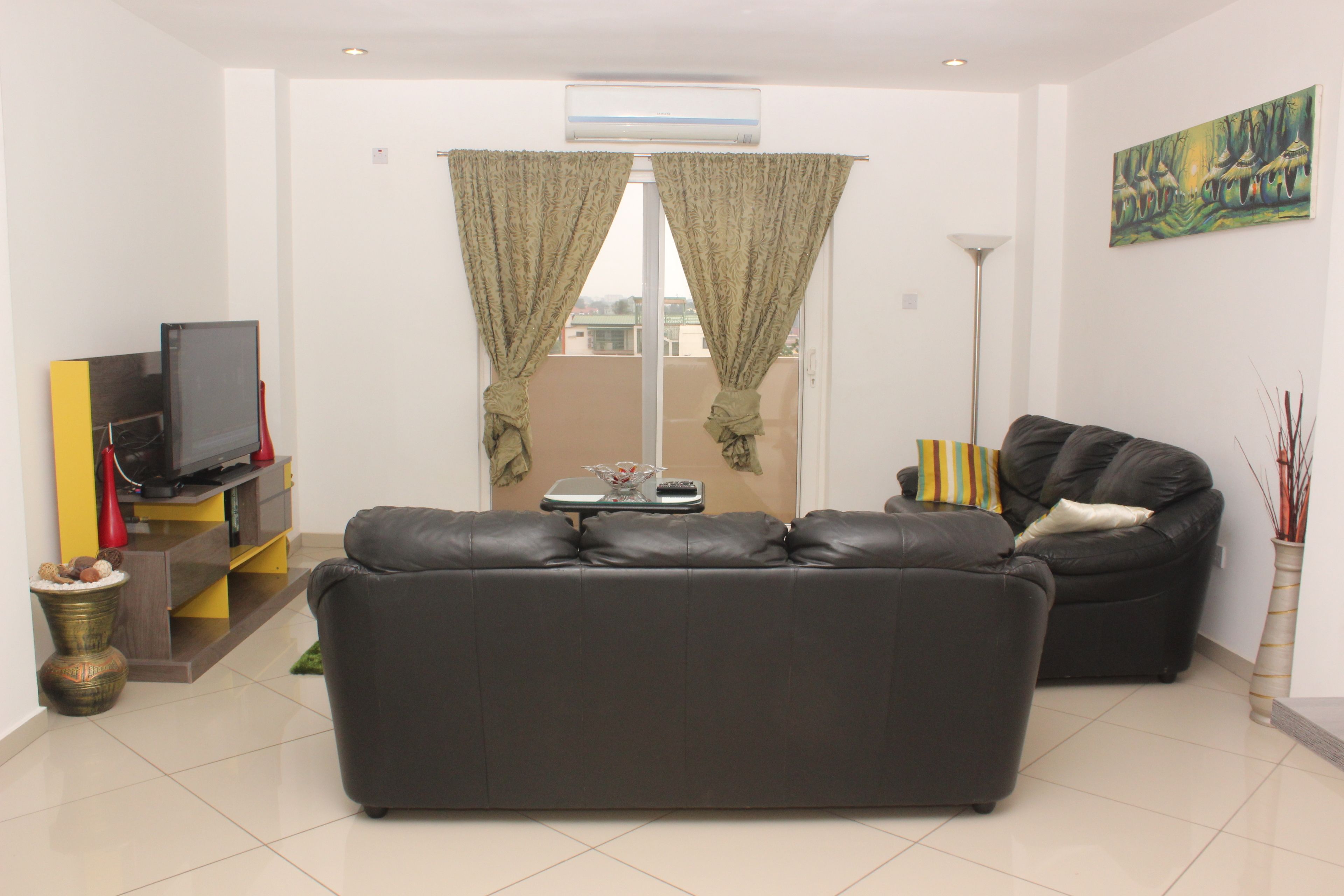 Una sala de estar moderna con un sofá de cuero negro, un televisor de pantalla plana y una mesa de comedor con sillas.