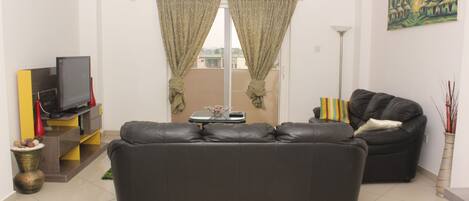 A modern living room with a black leather sofa, a flat-screen TV, and a dining table with chairs.