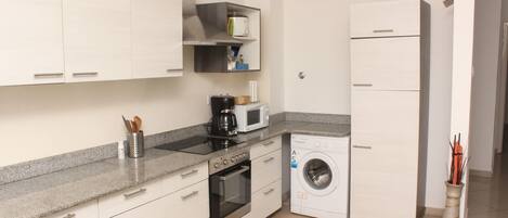 Cocina compacta con armarios blancos, microondas, cafetera y lavadora.
