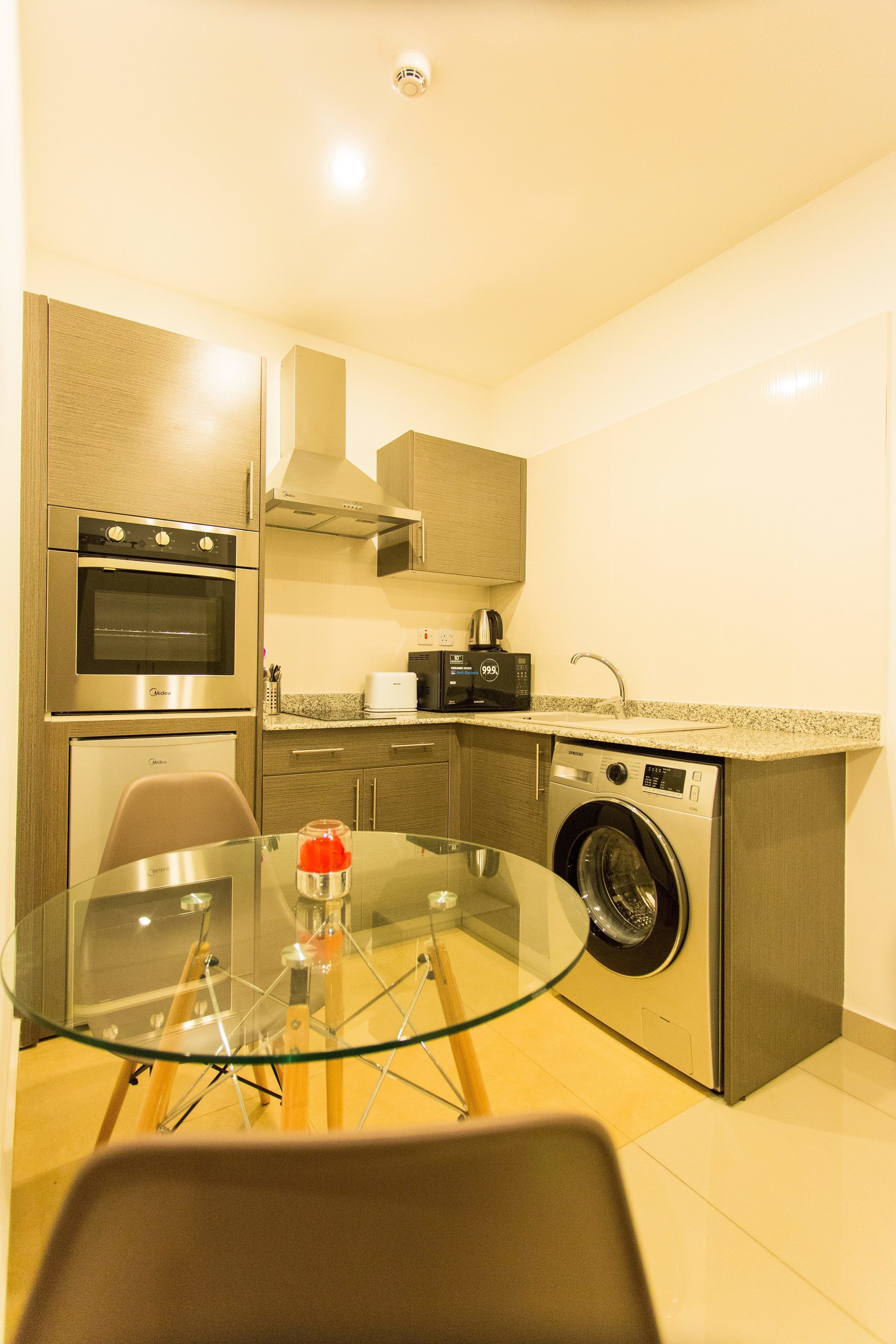 A compact kitchen with stainless steel appliances, a glass dining table, and a washing machine.
