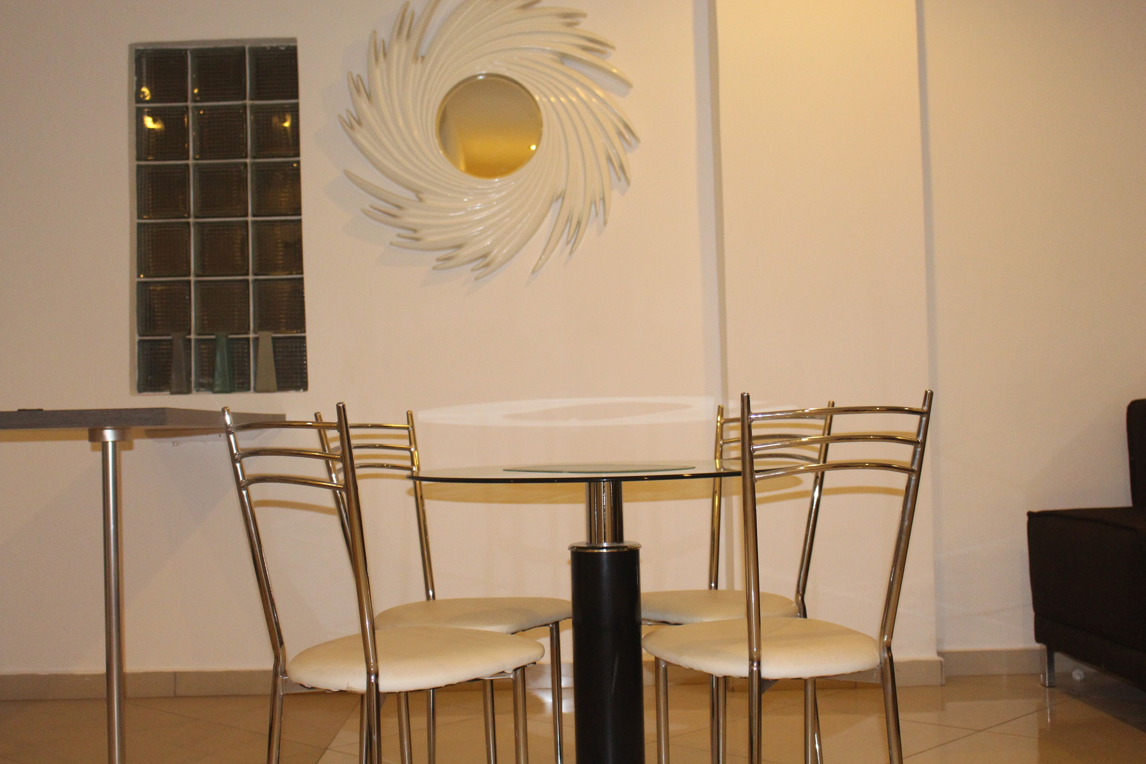 Un coin repas comprenant une table en verre et quatre chaises, un élément décoratif mural et une fenêtre à motifs géométriques.