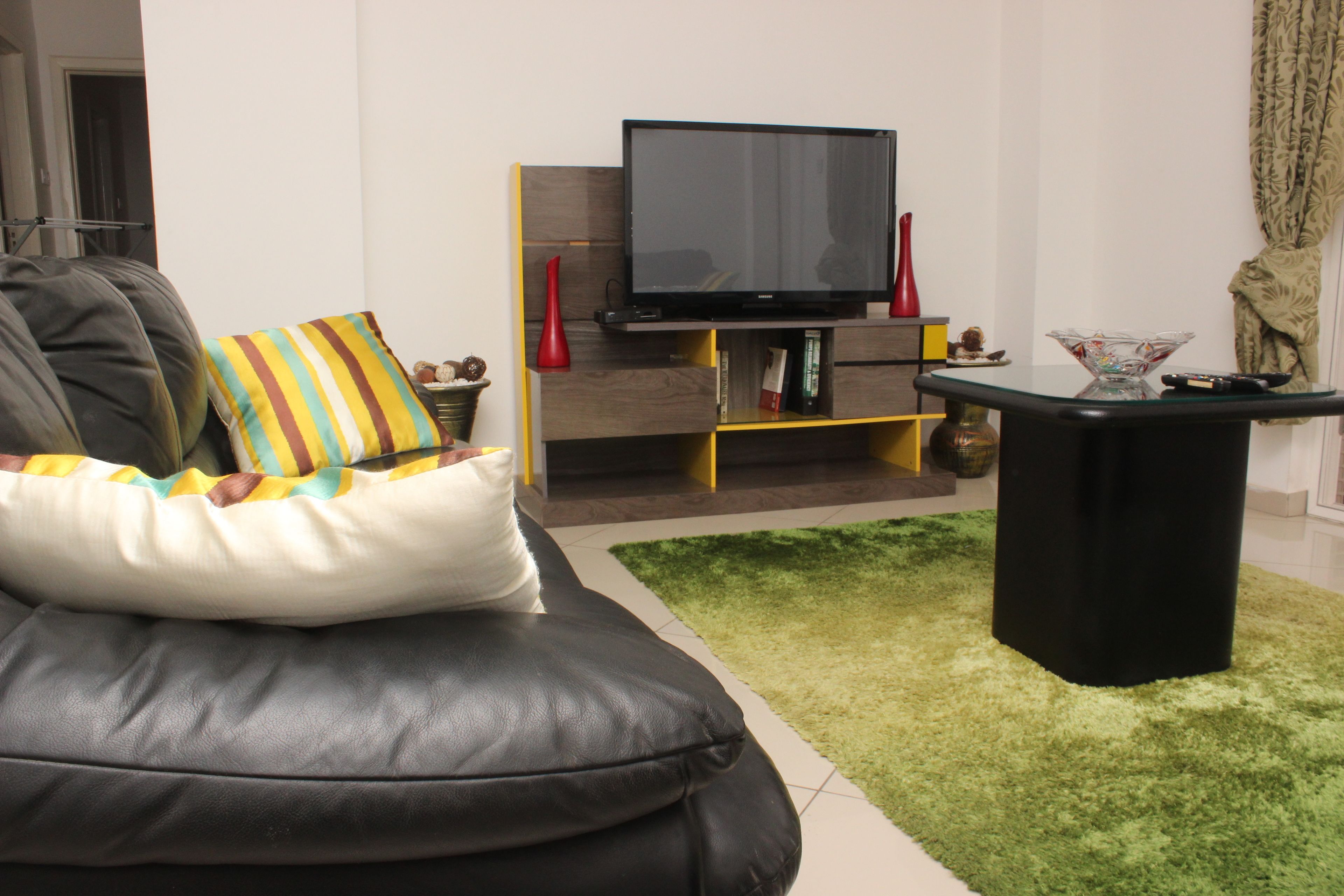 A modern living room with a black leather sofa, a flat-screen TV, and a glass coffee table.