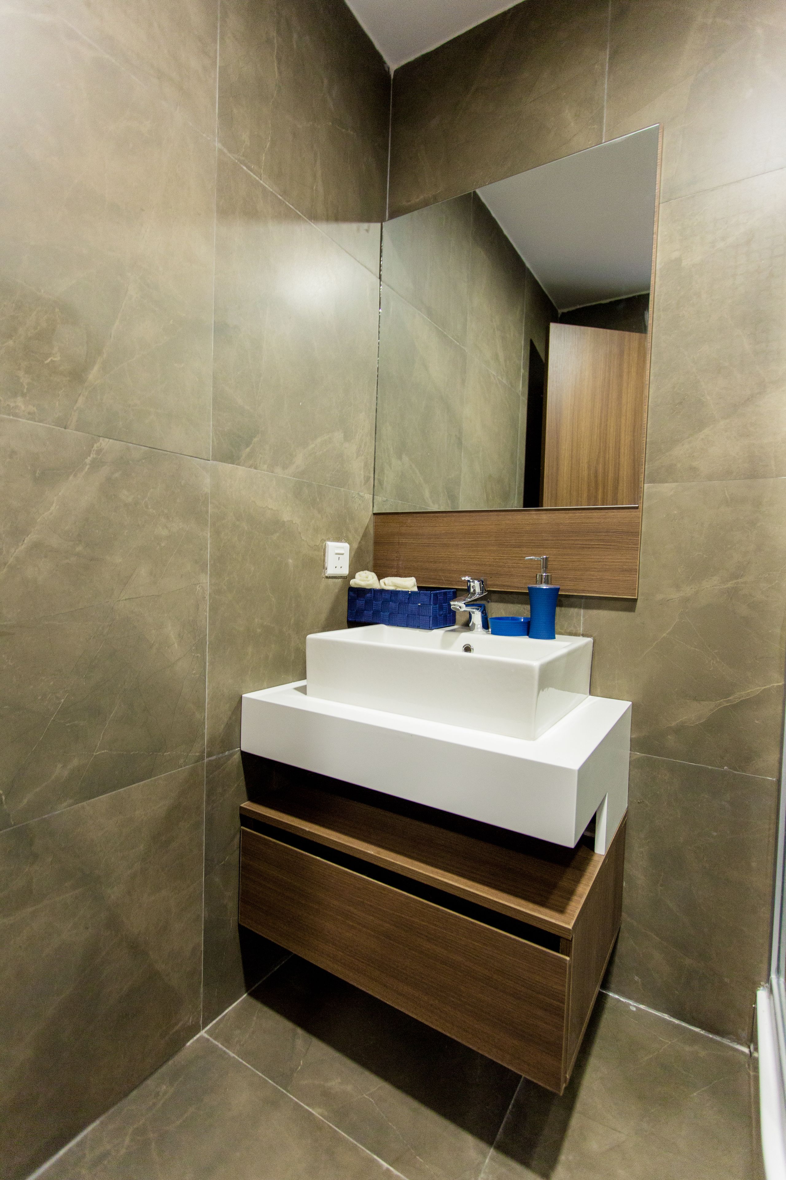 A modern bathroom with a white sink, blue soap dispenser, and wooden cabinet.