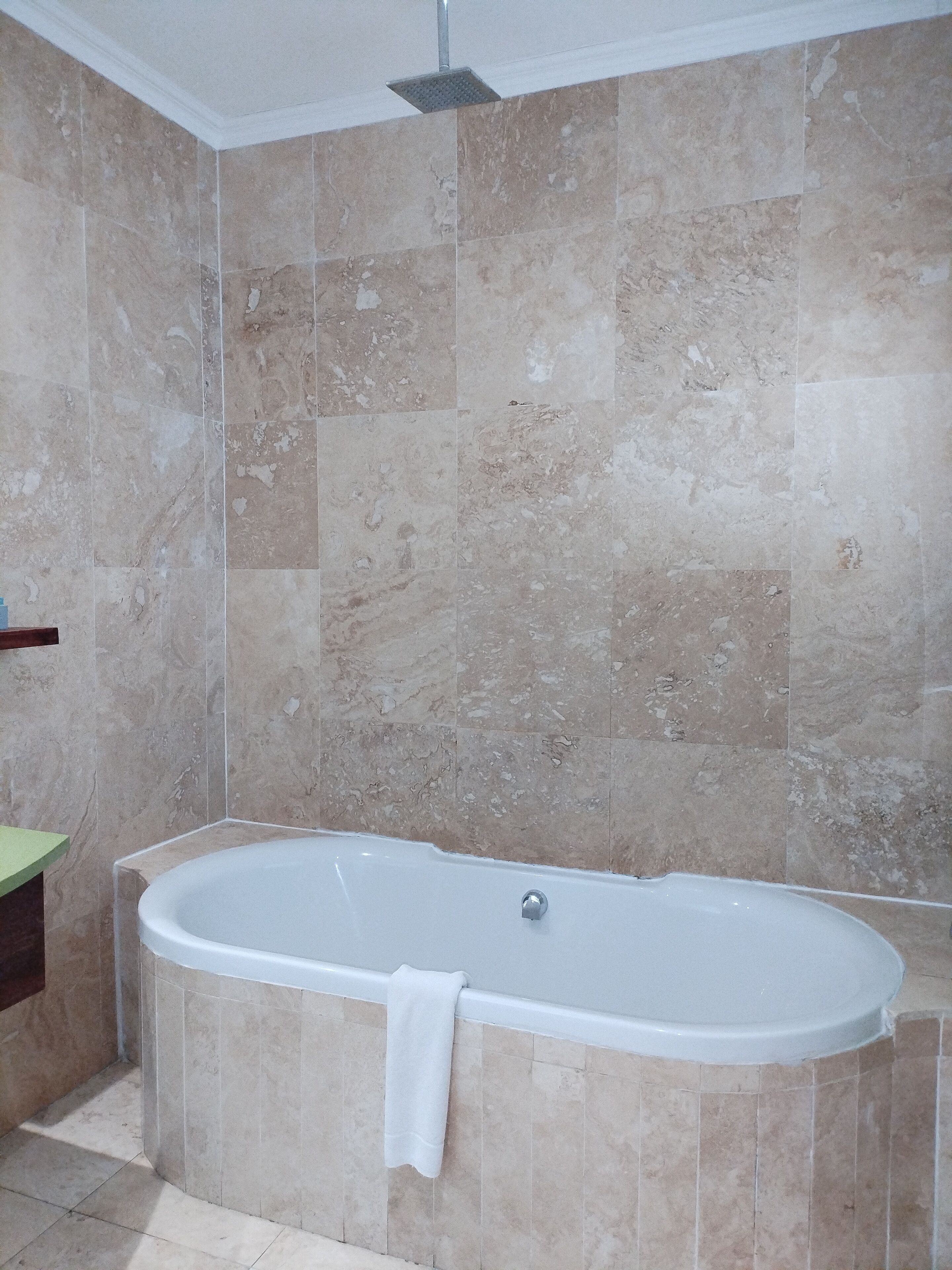 A bathroom with a freestanding bathtub, beige marble tiles, and a green countertop.