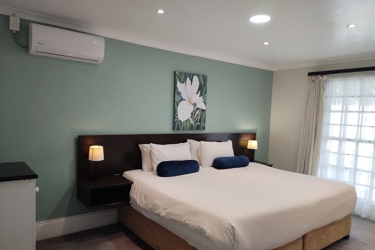 Ein Hotelzimmer mit einem großen Bett, zwei Nachttischen mit Lampen, einer Wand-Klimaanlage und einem Fenster mit Vorhängen.