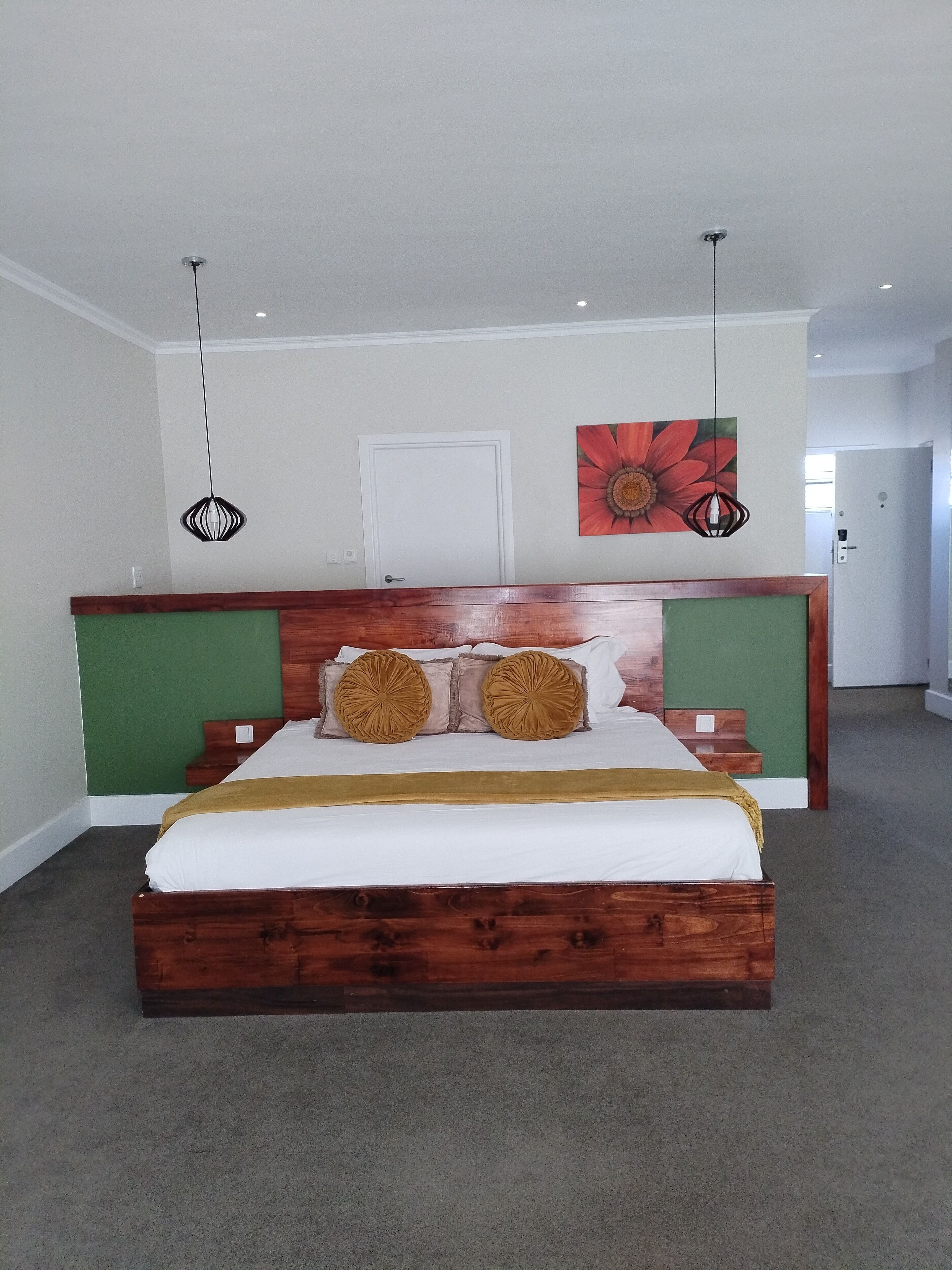 Un dormitorio con una cama de madera, paredes de acento verde y una obra de arte floral grande.