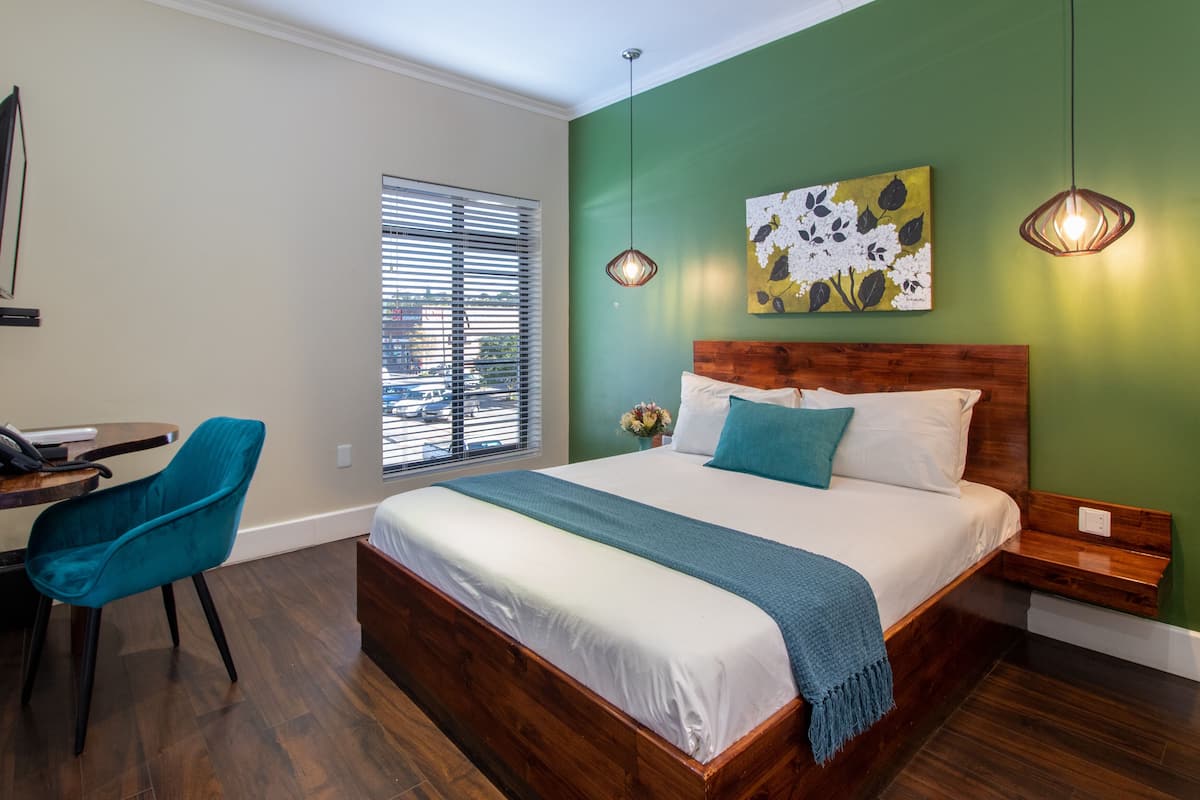 Ein Schlafzimmer mit einem hölzernen Bett, einem blauen Sessel, einem Fenster mit Jalousien und einer grünen Wand.