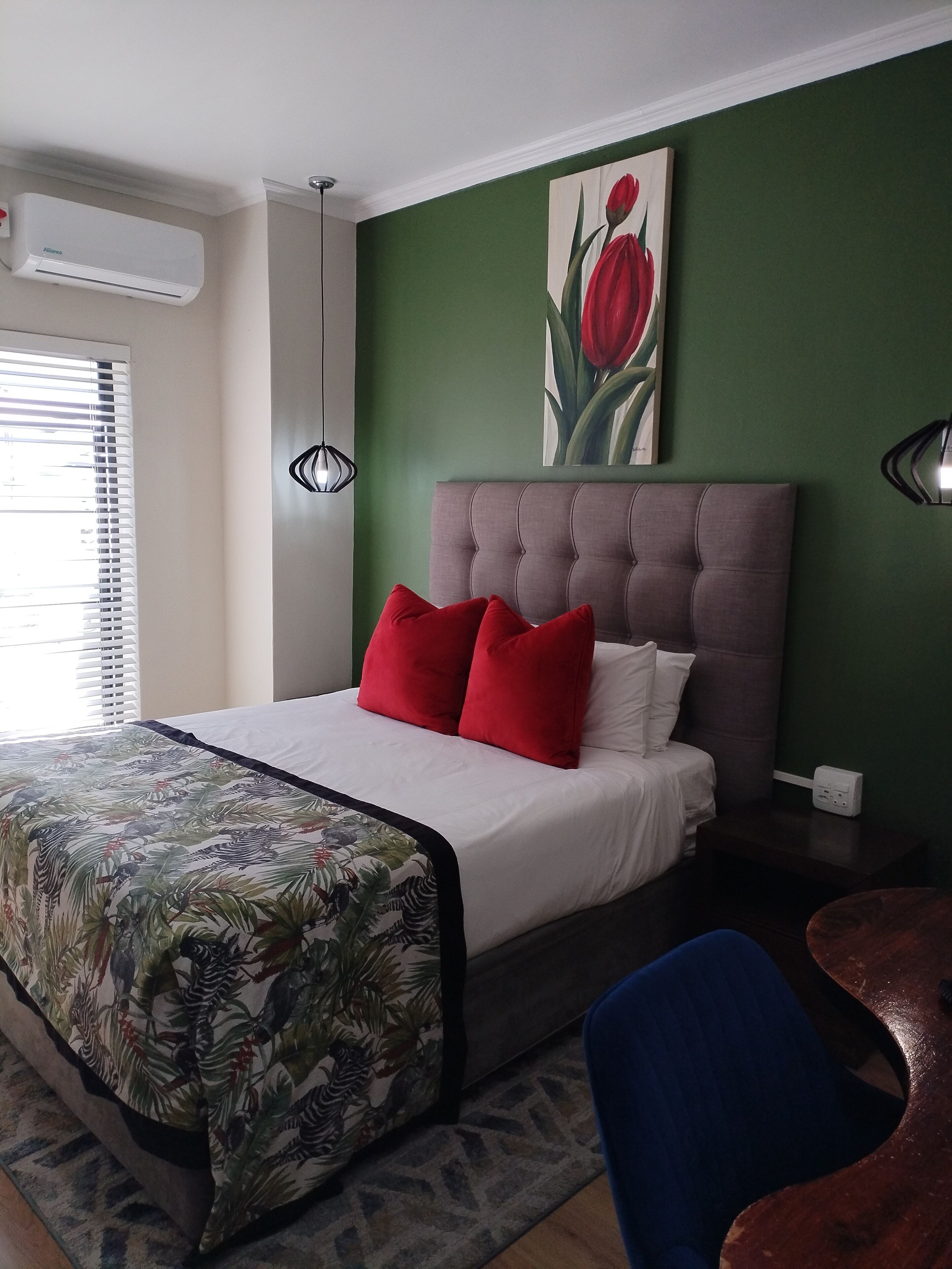 A bedroom with a bed, green walls, a red tulip painting, and a window with blinds.