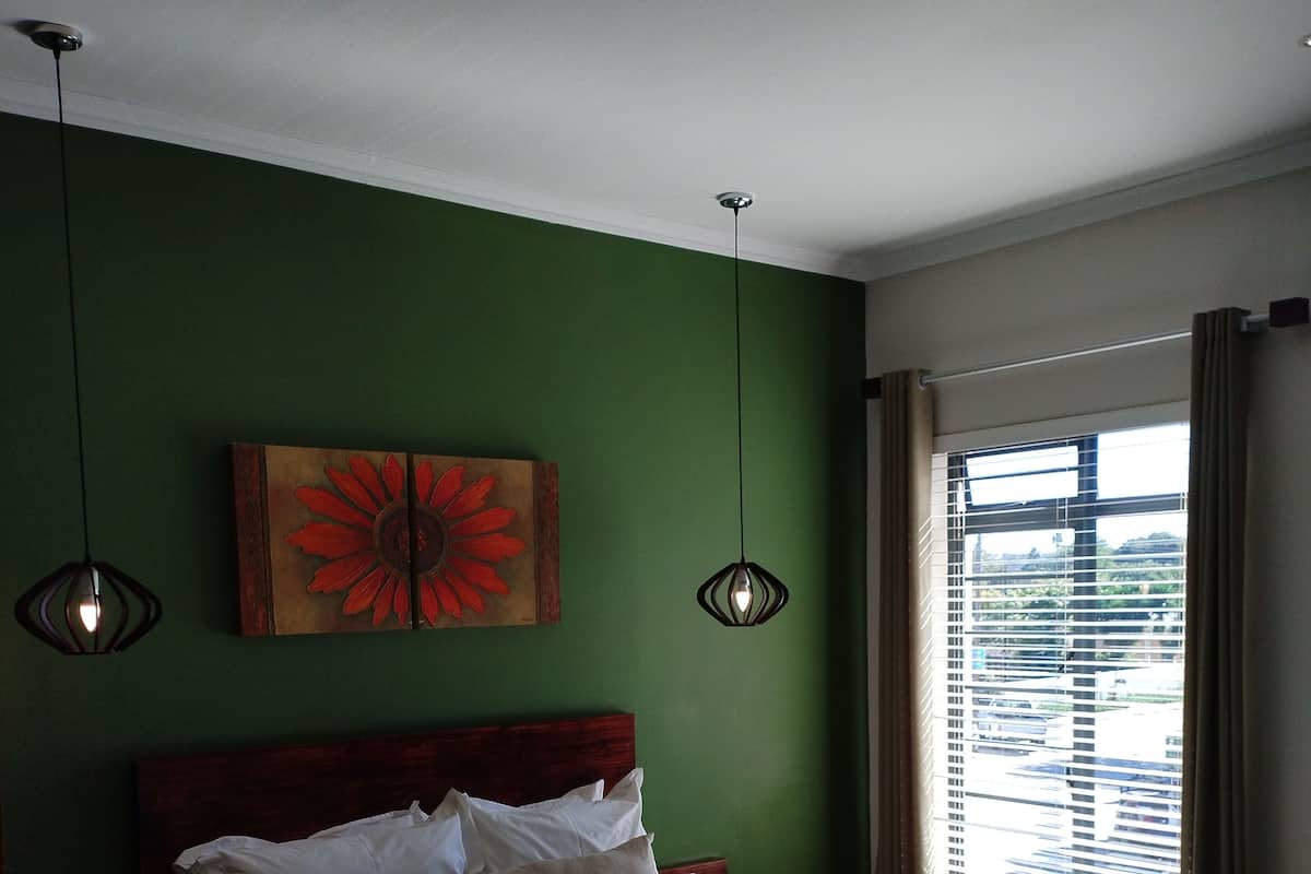 Ein Schlafzimmer mit einem großen Bett, grünen Wänden, einem Holzkopfschild, zwei Pendelleuchten und einem Fenster mit Jalousien.