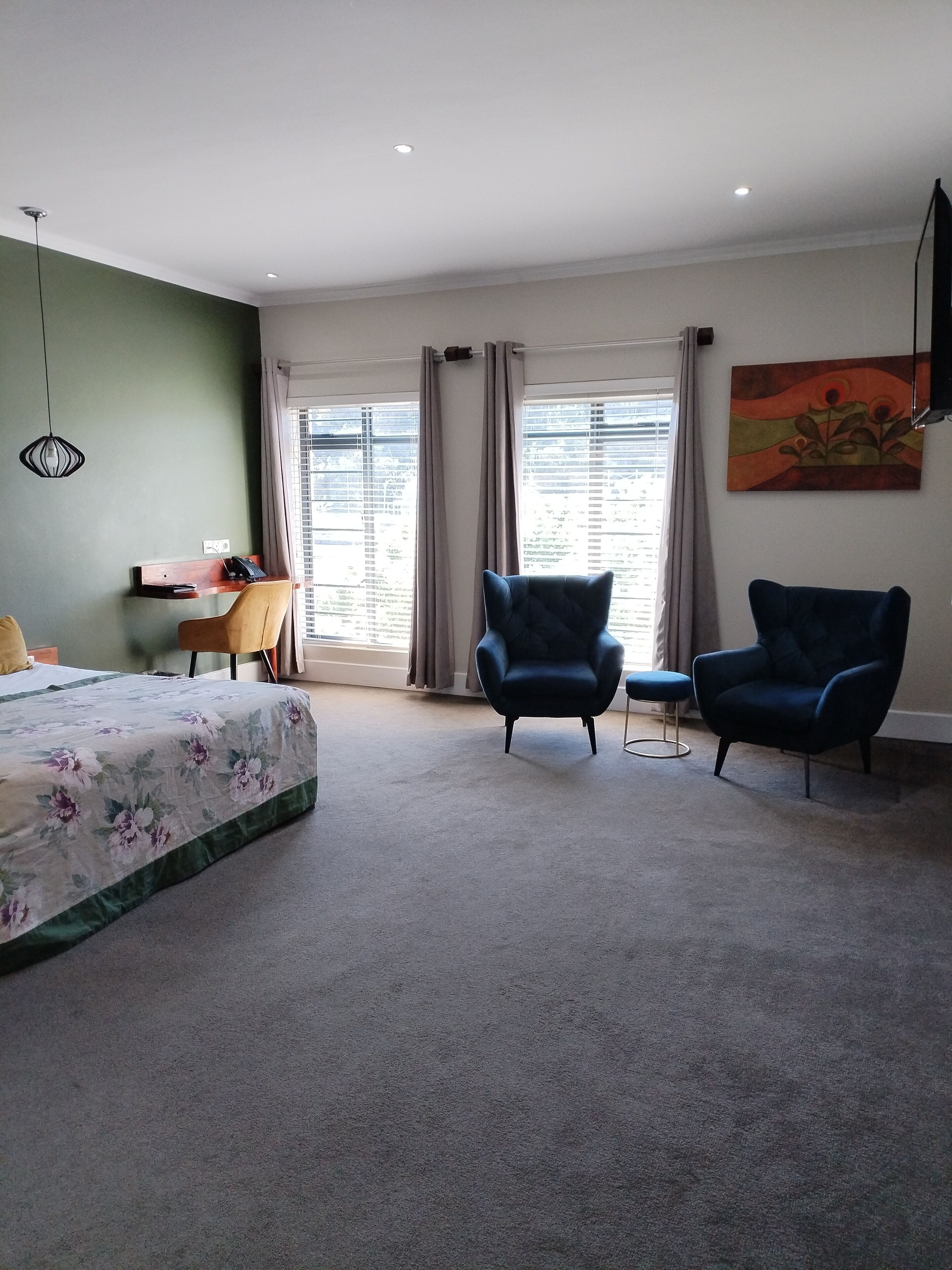 A bedroom with a bed, two armchairs, a desk, and a painting on the wall.