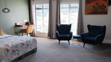 A bedroom with a bed, two armchairs, a desk, and a painting on the wall.