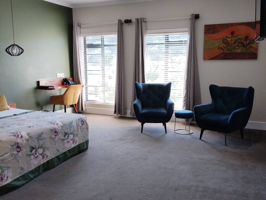 A bedroom with a bed, two armchairs, a desk, and a painting on the wall.