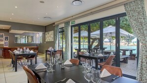 A restaurant with tables set for dining, large windows overlooking a pool area.