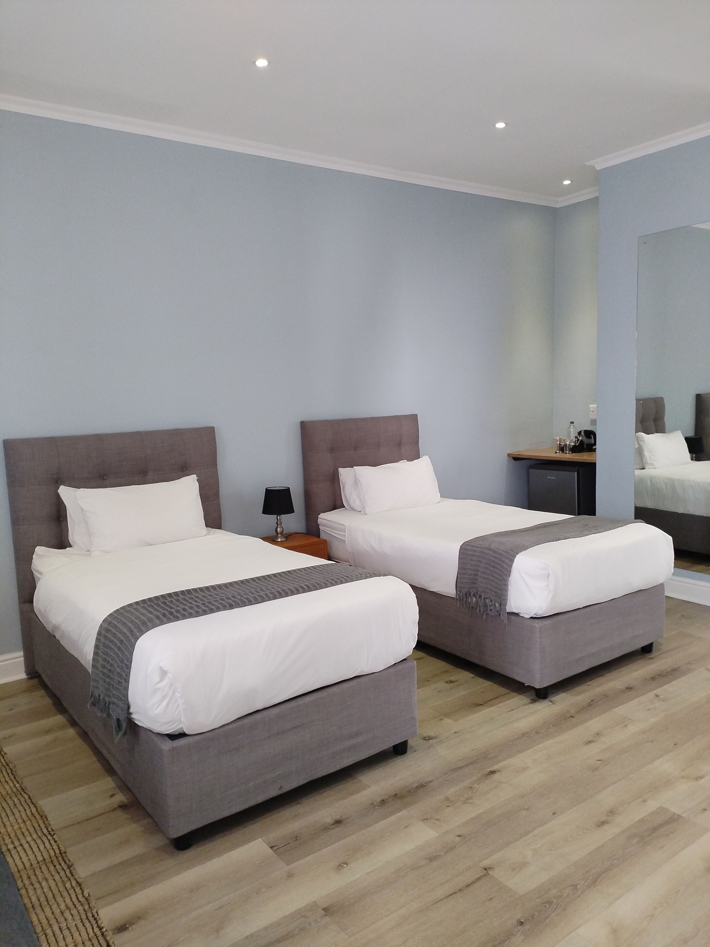 Una habitación de hotel con dos camas, una mesita de noche, una lámpara y un espejo.