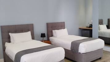 A hotel room with two beds, a nightstand, a lamp, and a mirror.