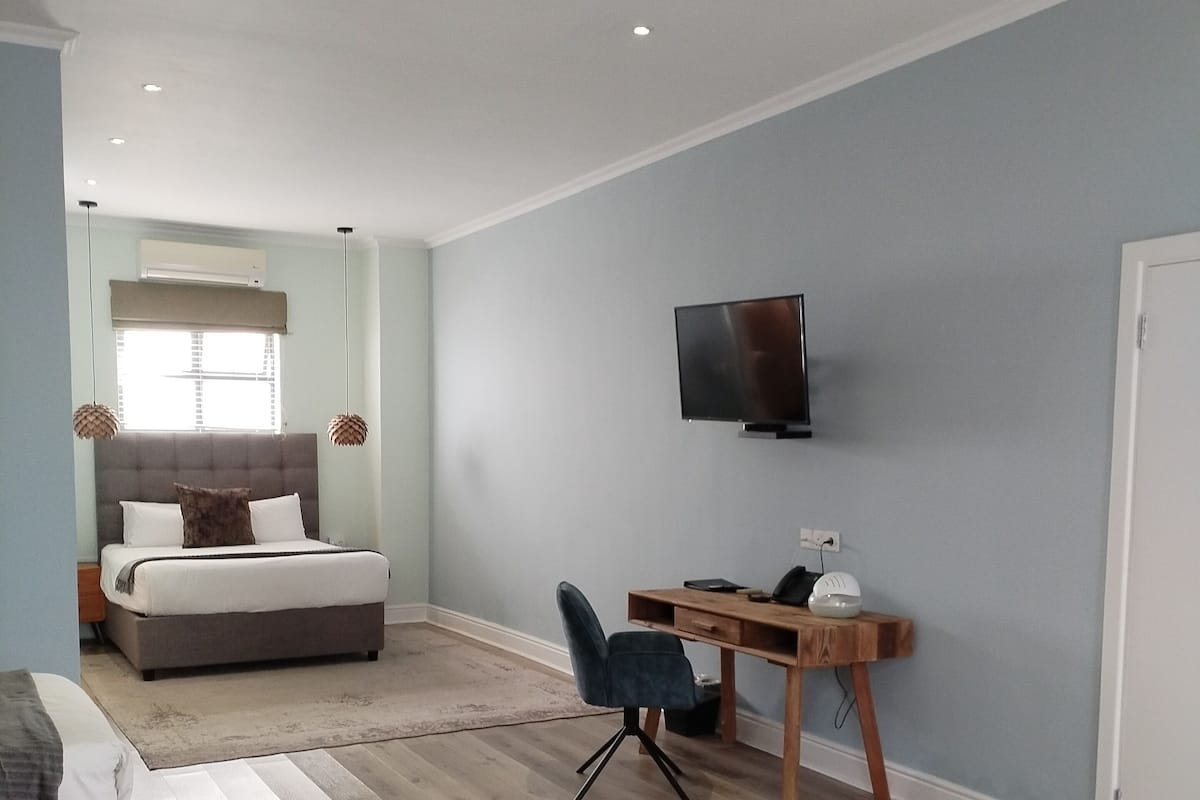 Ein Schlafzimmer mit einem Bett, einem Schreibtisch, einem Stuhl, einem Fernseher und einem Fenster.