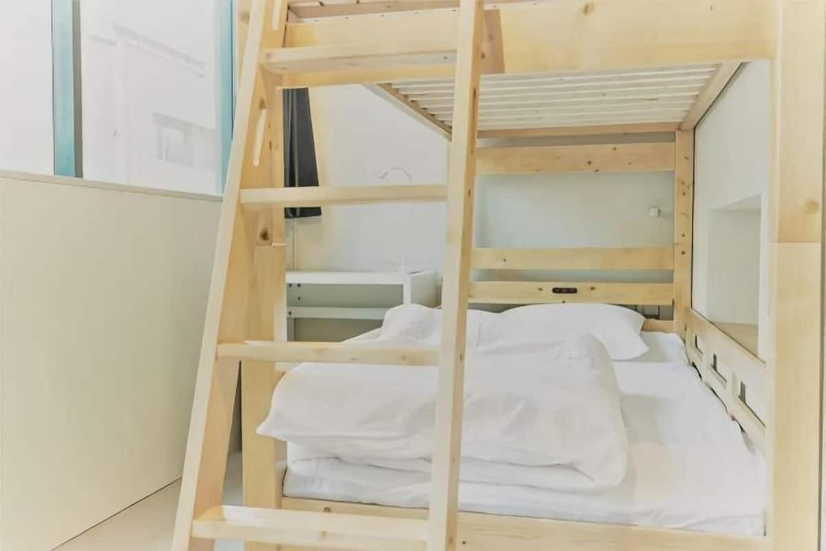 A bunk bed with a wooden ladder, a white mattress, and a small shelf.