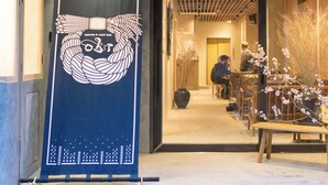 A hallway with a blue banner, wooden benches, and a potted plant. - obi Hostel (Tokyo)