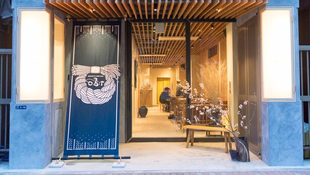 A building entrance with a wooden pergola, a large decorative banner, and indoor seating area with tables and chairs. - obi Hostel (Tokyo)
