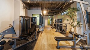 A gym with various exercise equipment, a wooden floor, and a visible clock on the wall. - obi Hostel (Tokyo)