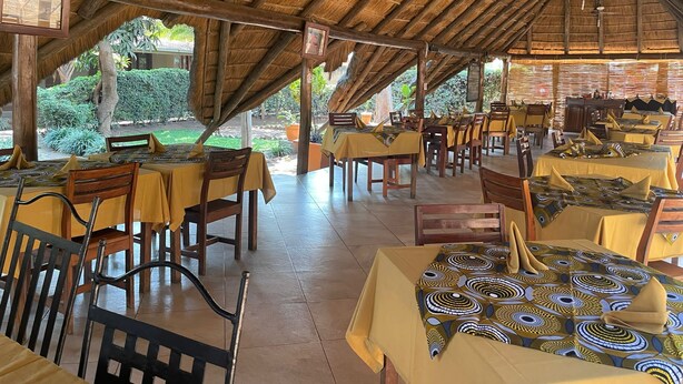 An outdoor restaurant with thatched roofs and wooden tables and chairs.