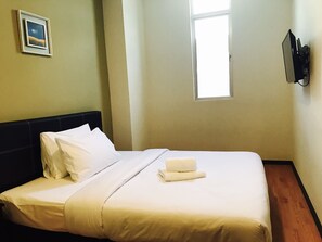 A neatly made bed with white linens, a small window with daylight, and a wall-mounted TV. - Gem Hotel Nusajaya (Johor Bahru)