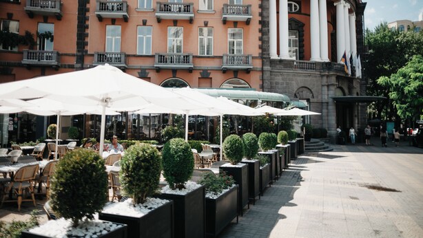 A hotel with outdoor seating, white umbrellas, and a grand entrance with columns. - Grand Hotel Yerevan (Yerevan)