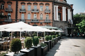 Un hotel con terraza al aire libre, sombrillas blancas y una entrada imponente con columnas.