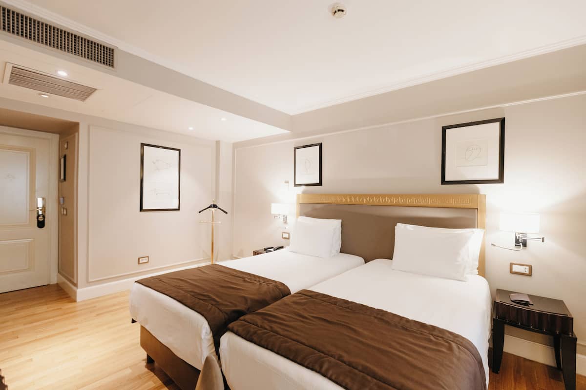 A hotel room with two beds, a wooden headboard, a bedside table, and a framed picture on the wall.