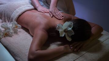 Iemand ontvangt een rugmassage op een massagetafel, met een handdoek en bloemen.