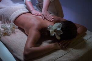 Iemand ontvangt een rugmassage op een massagetafel, met een handdoek en bloemen.