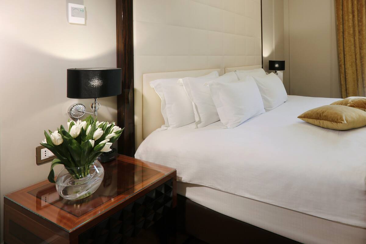 A hotel room with a large bed, a bedside table with a lamp, and a vase of flowers.
