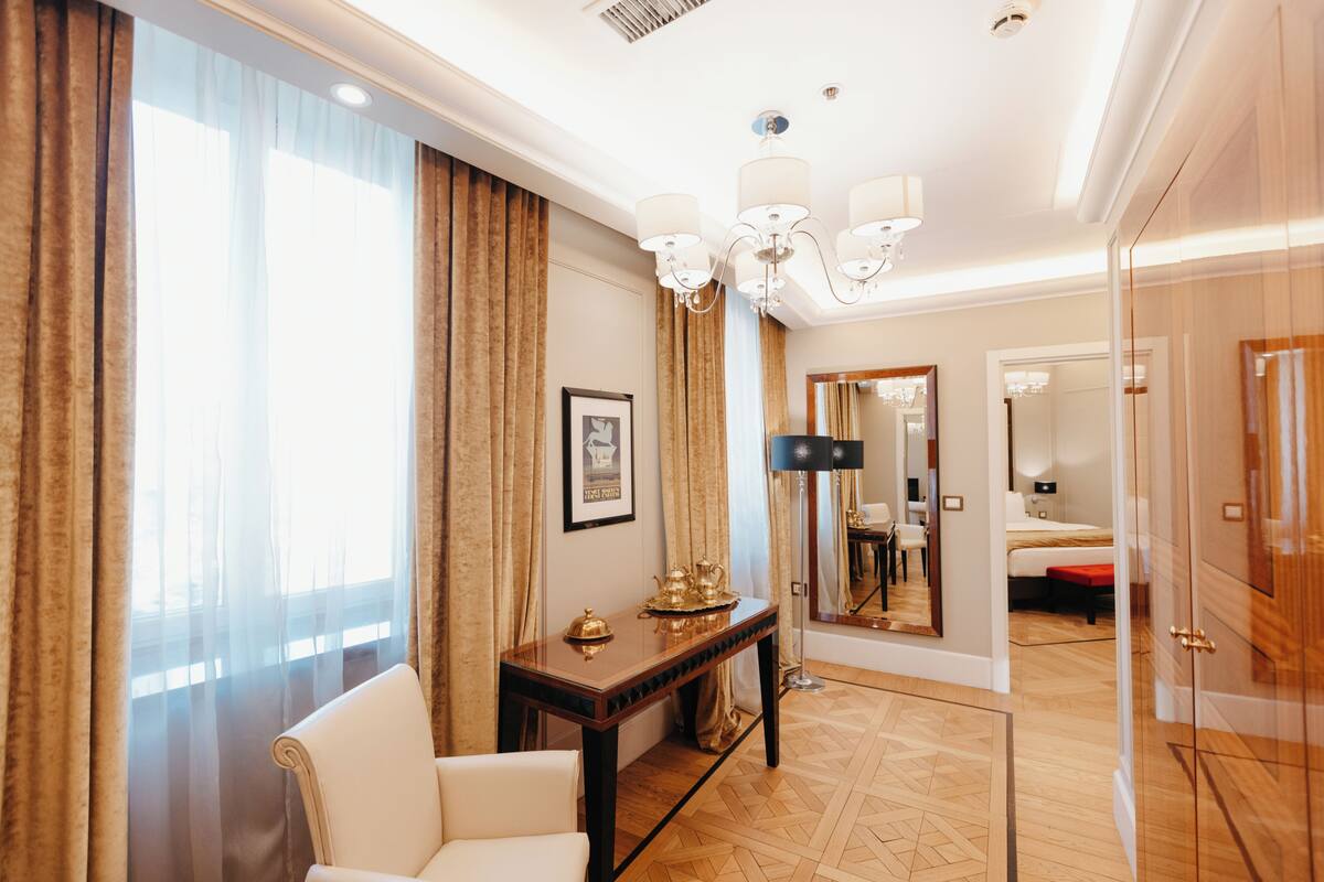 A hotel room with a large window, a sitting area with a chair and a table, a bed, a mirror, and a wardrobe.