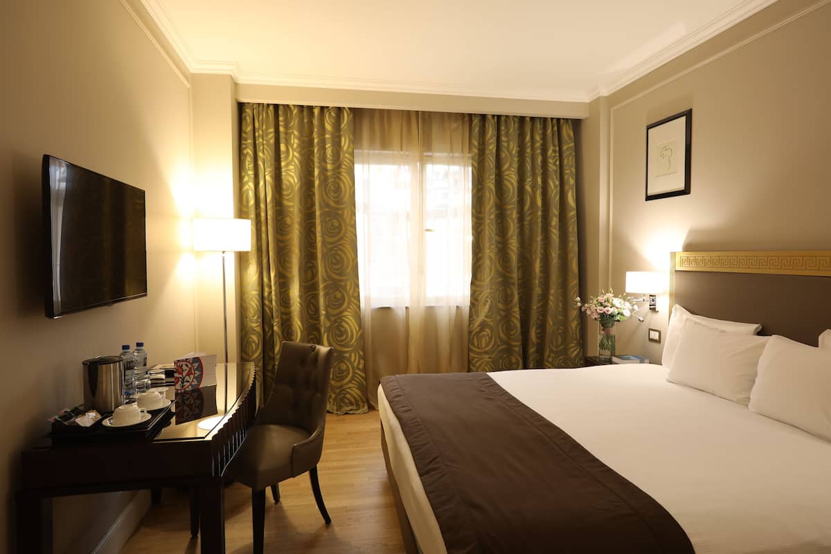 A hotel room with a large bed, a desk with a chair, a television, and a window with curtains.