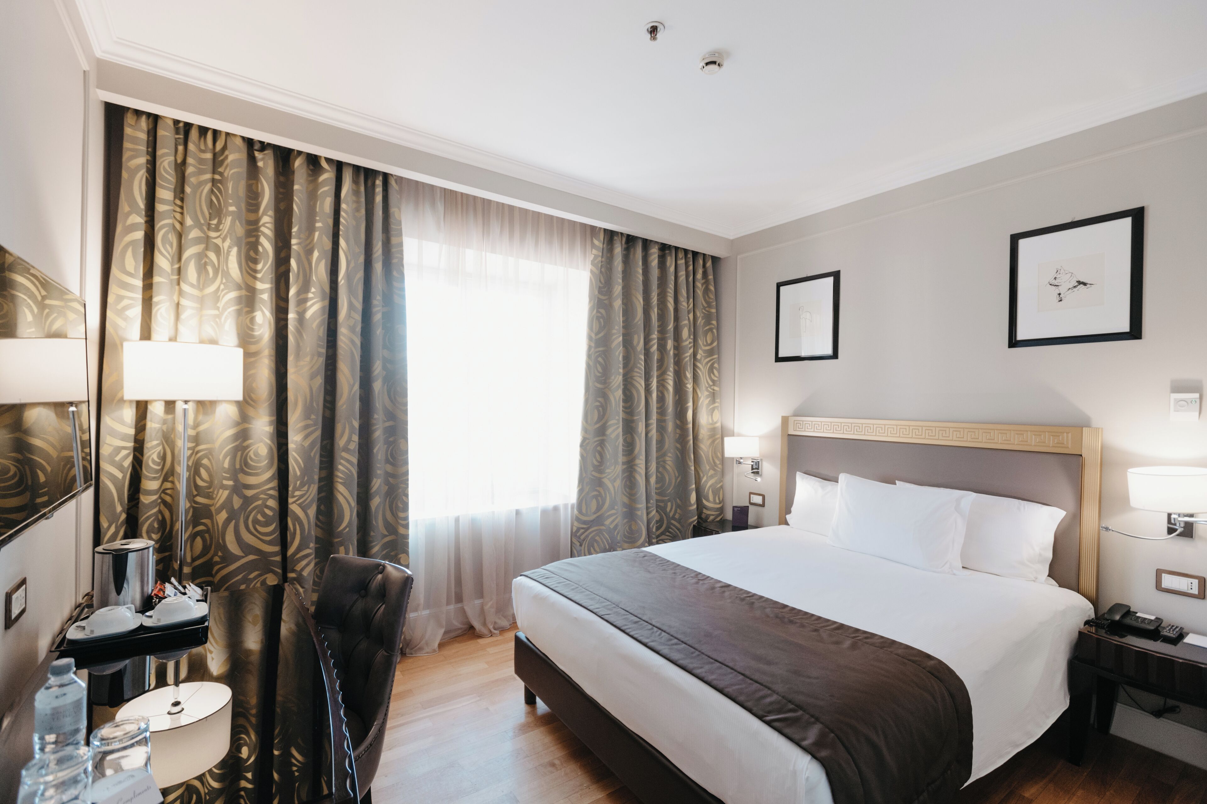 Une chambre d’hôtel avec un grand lit, un bureau avec une lampe, une chaise et une fenêtre avec des rideaux.