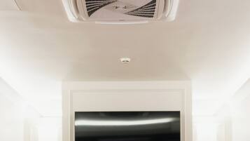 Een vergaderzaal met een grote tafel, zes stoelen, een flatscreen televisie en een ventilatie rooster in het plafond.