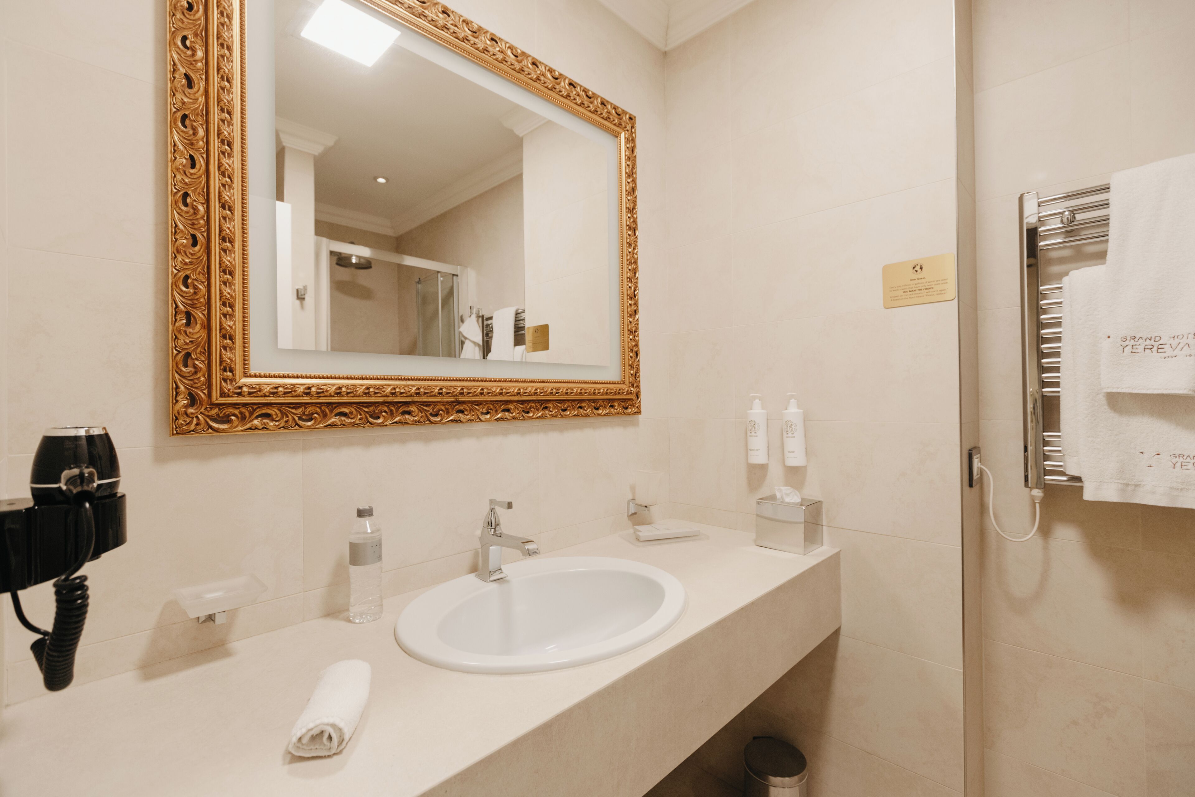 Een hotelbadkamer met een grote, versierde spiegel, een witte wastafel, een handdoek en toiletartikelen.