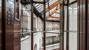 An elevator with a red carpet and a view of a multi-level atrium with plants and artwork. - Grand Hotel Yerevan (Yerevan)