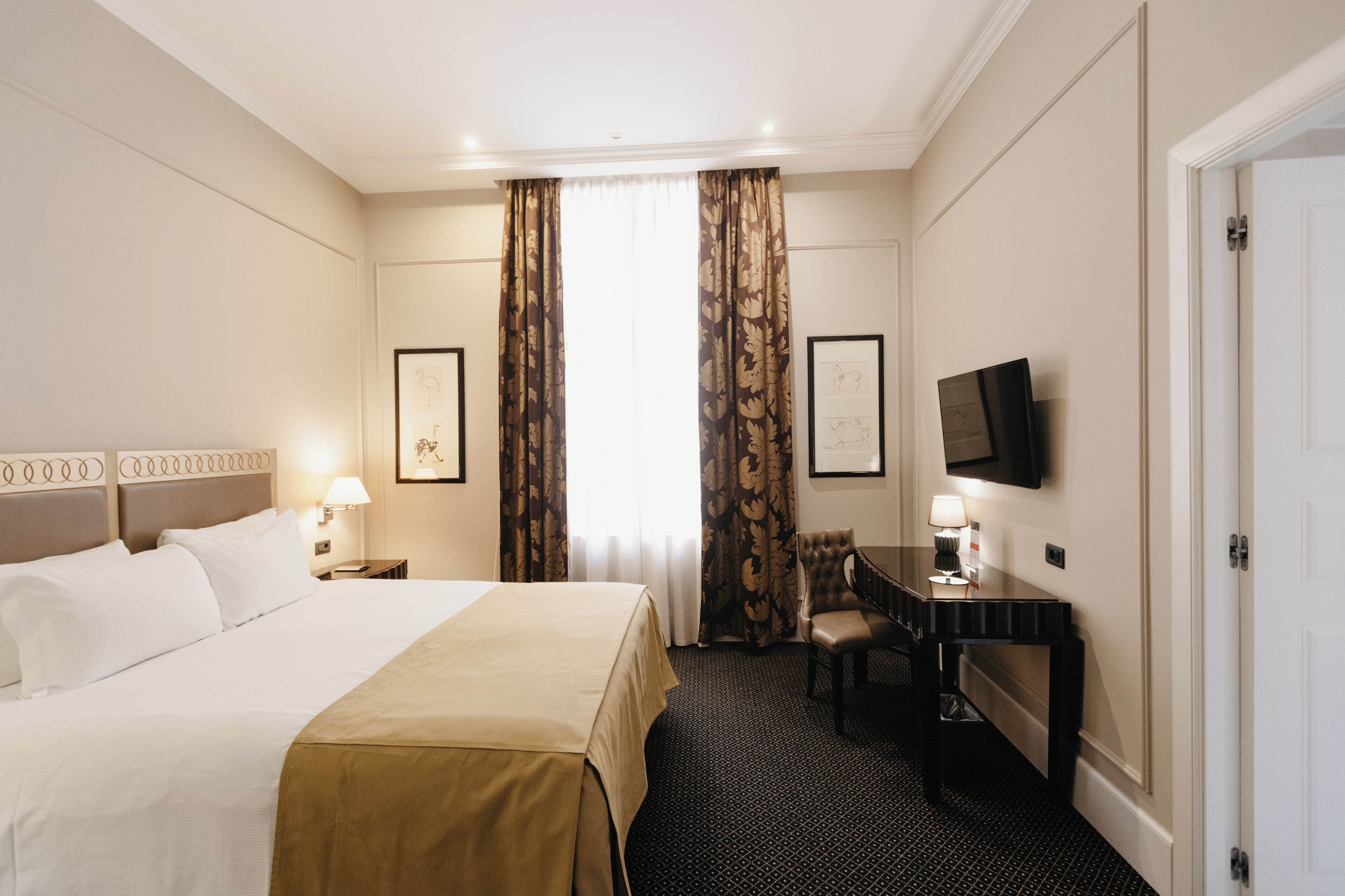 Une chambre d’hôtel avec un grand lit, un bureau, une chaise, une télévision et des œuvres d’art encadrées accrochées aux murs.