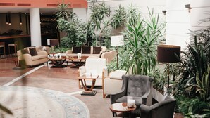 A spacious lobby with multiple seating areas, a large circular rug, and abundant indoor plants. - Grand Hotel Yerevan (Yerevan)