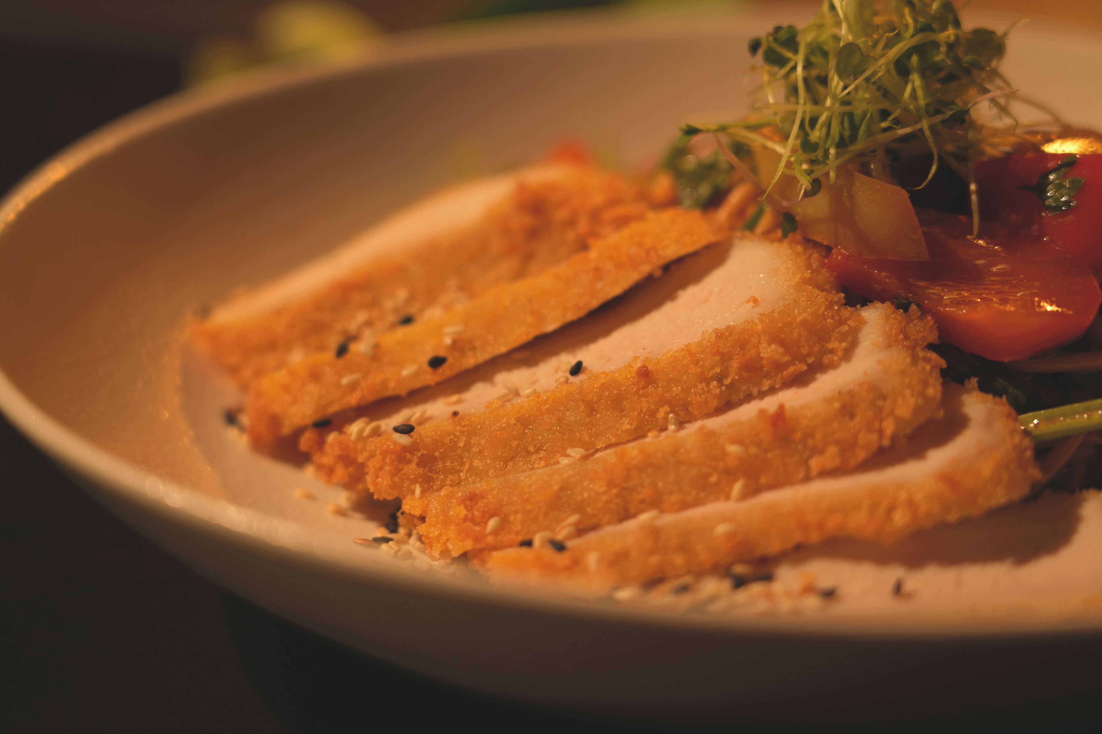A plate with a breaded and sliced food item, possibly chicken, accompanied by a small salad and a slice of tomato.