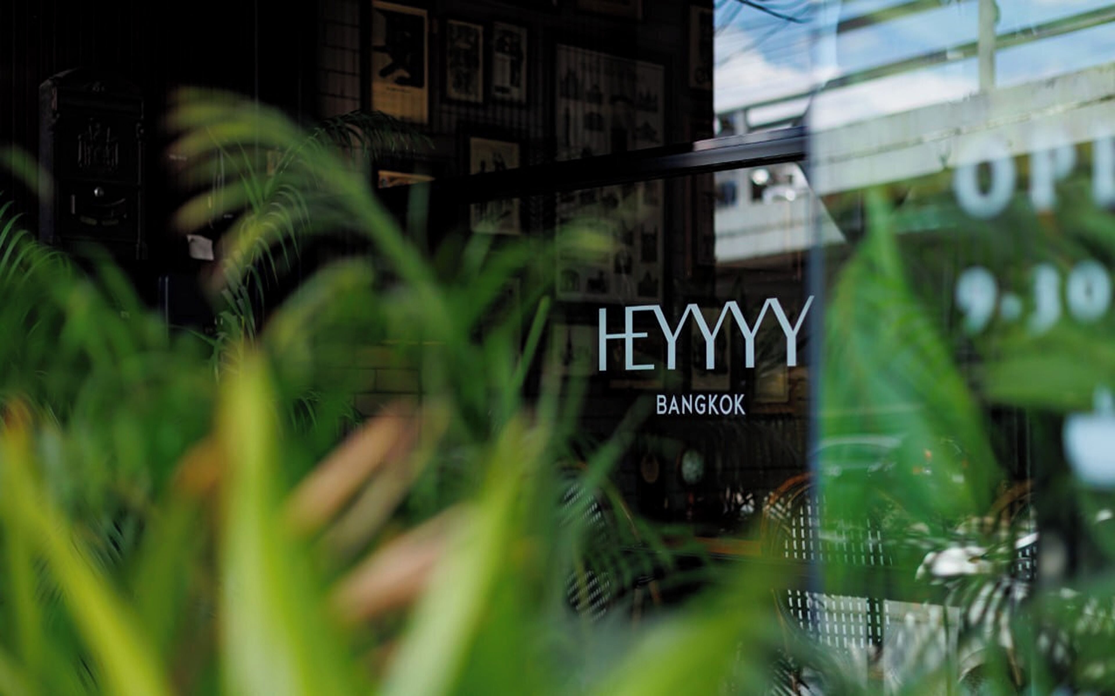 A view through a window with the text "HEYYYY BANGKOK" visible, surrounded by greenery.